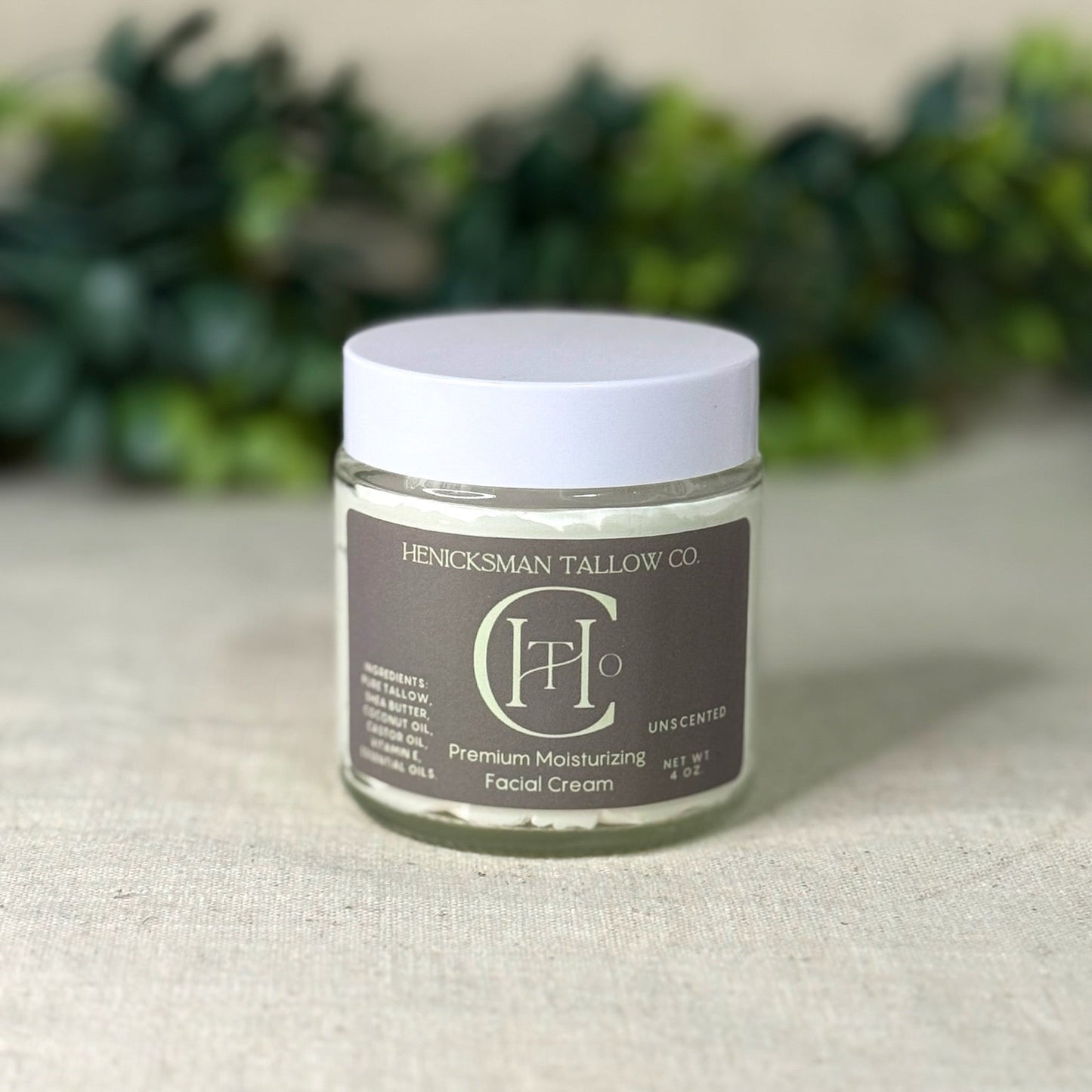 Jar of Henicksman Tallow Co. facial cream on a textured surface with greenery in the background