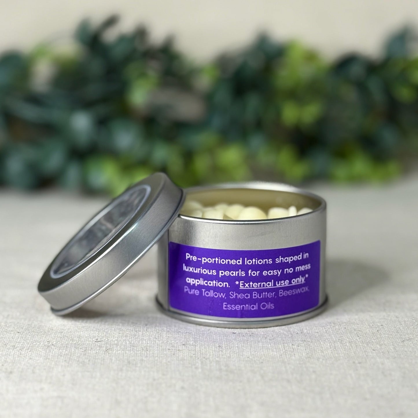Metallic tin with a purple label on a light surface with greenery in the background