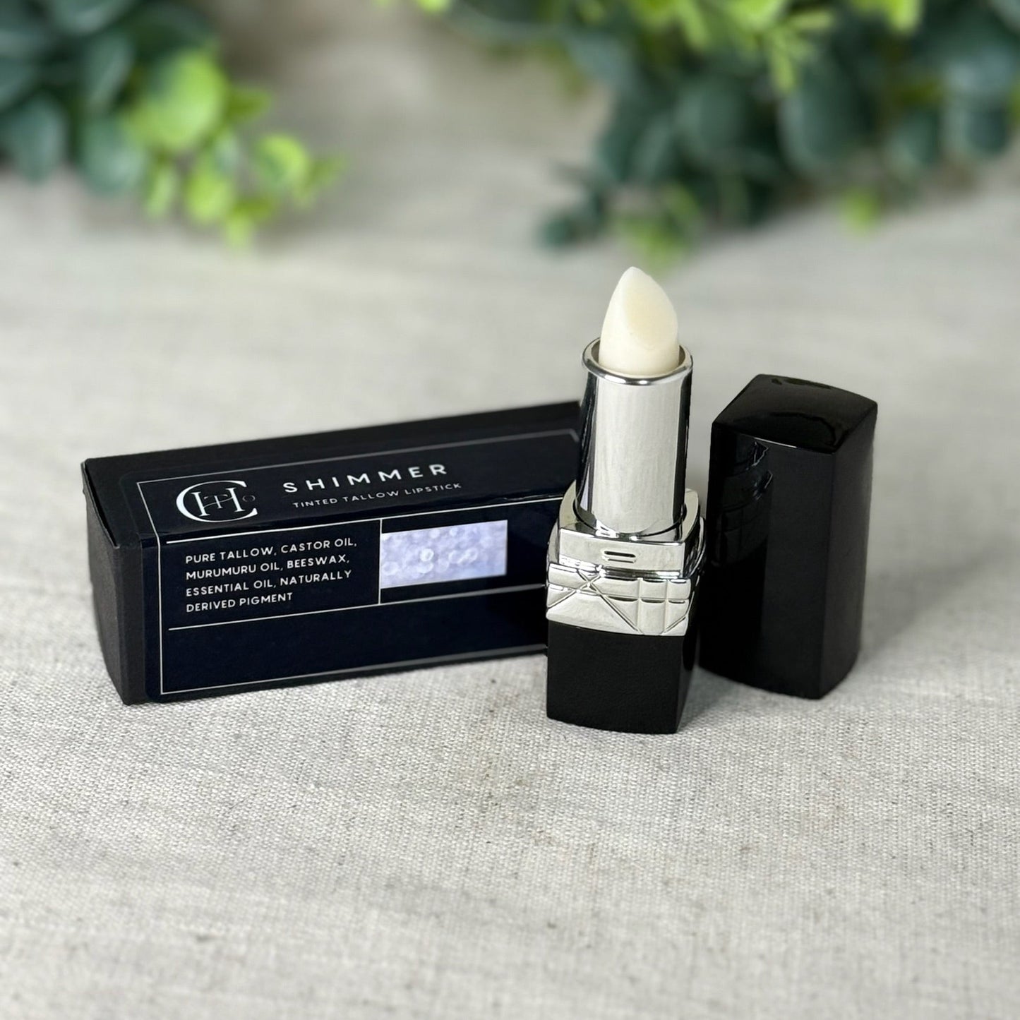 Lipstick with black packaging on a textured surface with greenery in the background