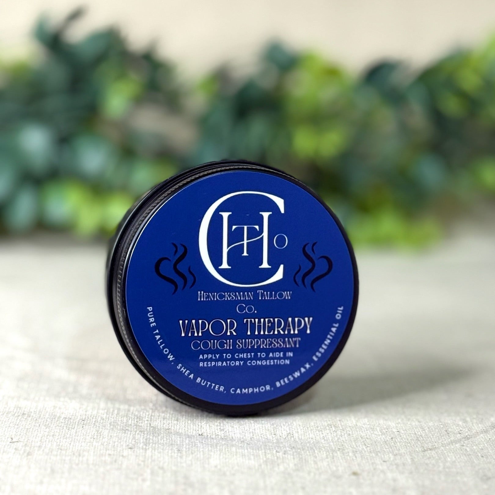 Blue container of vapor therapy product with brand logo on a white surface with greenery in the background