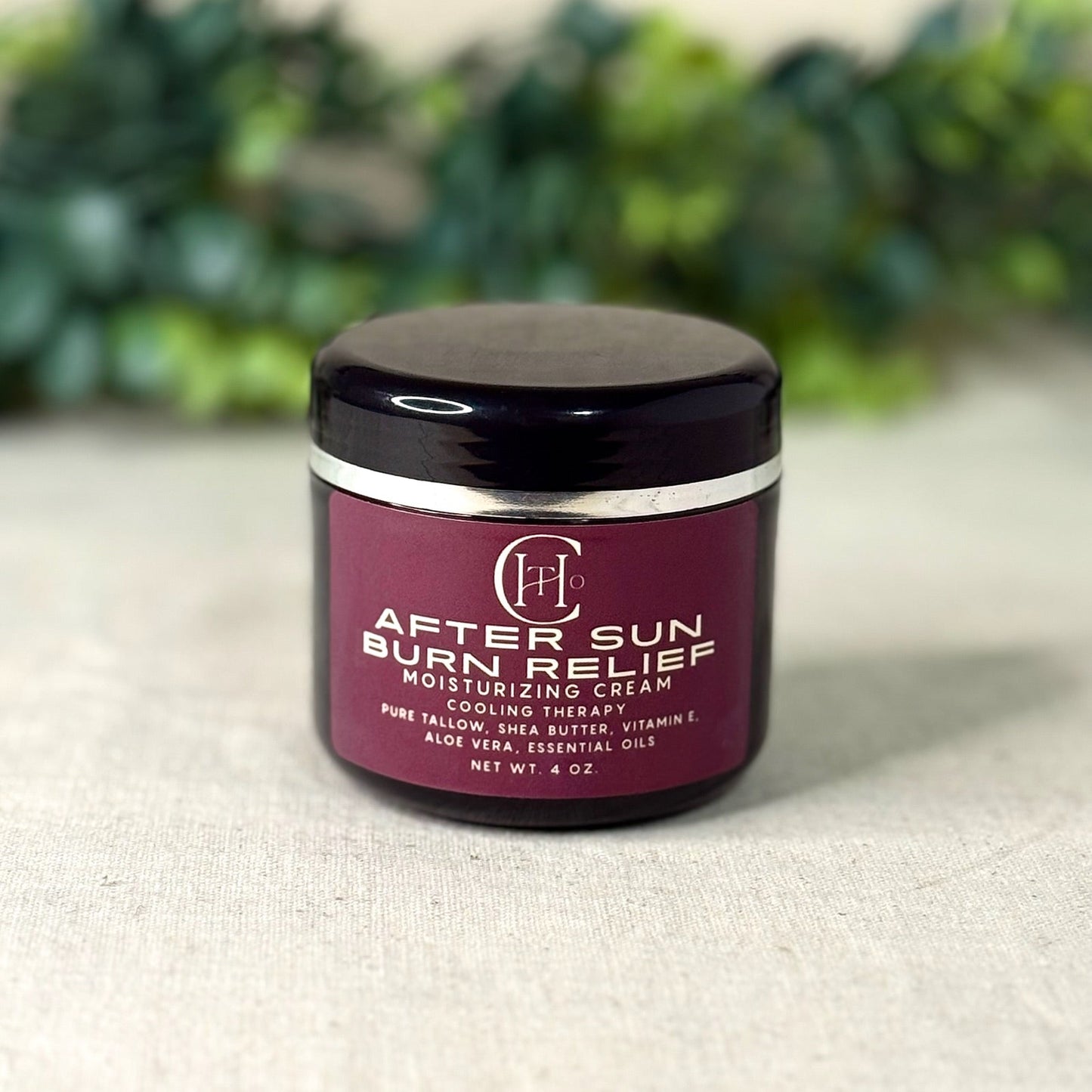 Jar of after-sun burn relief moisturizing cream on a textured surface with greenery in the background