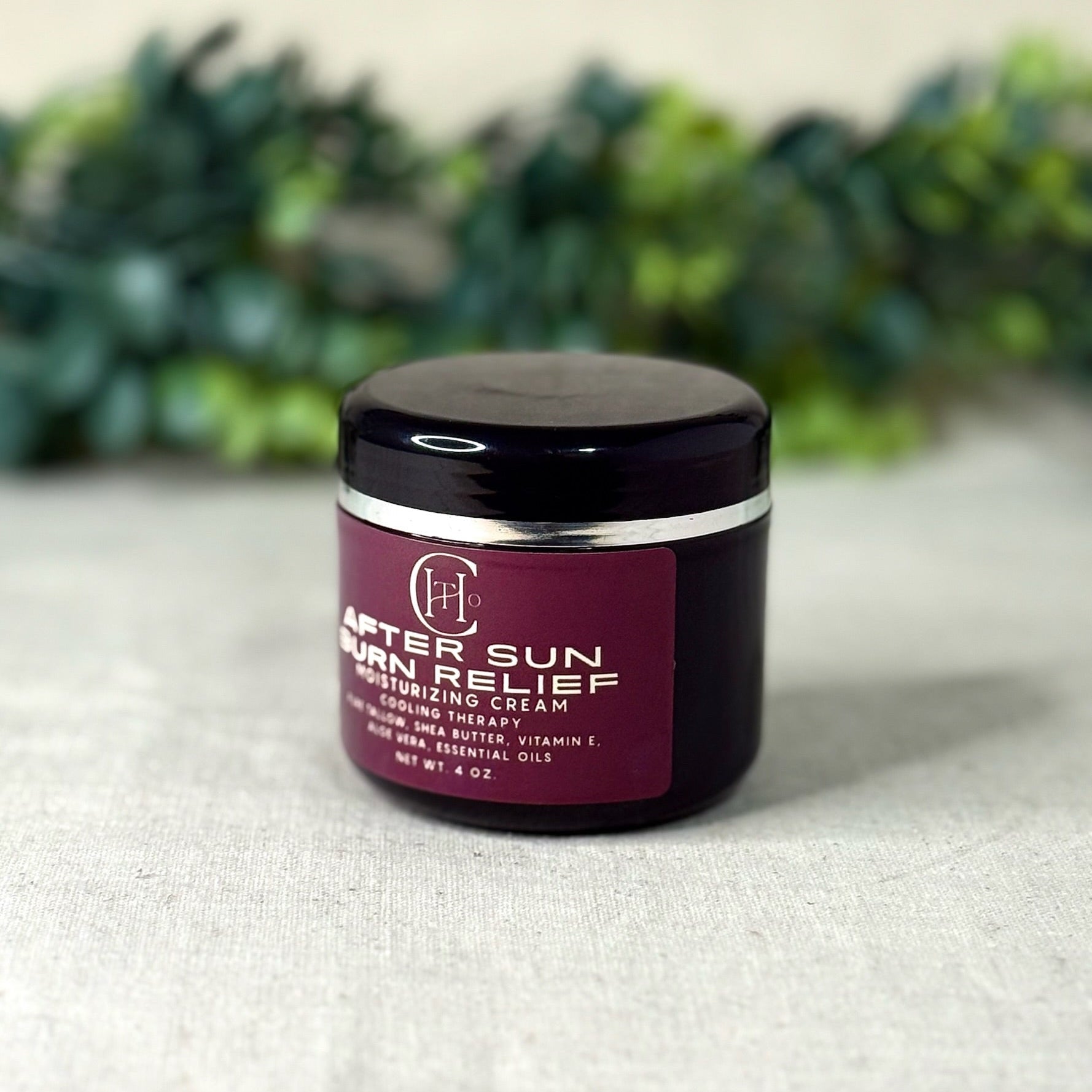 Jar of after sun relief cream on a textured surface with greenery in the background