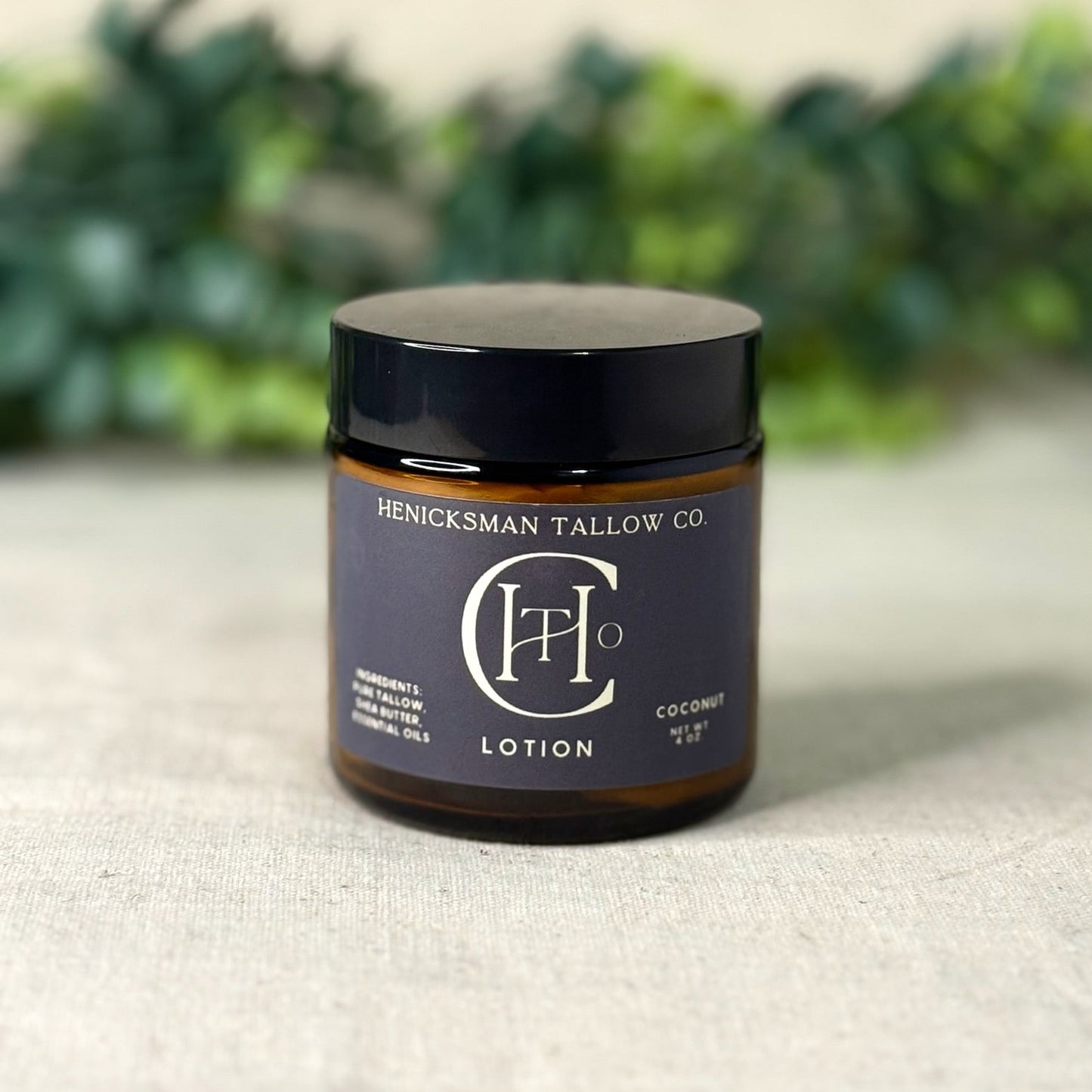 Jar of Henicksman Tallow Co. lotion on a textured surface with greenery in the background