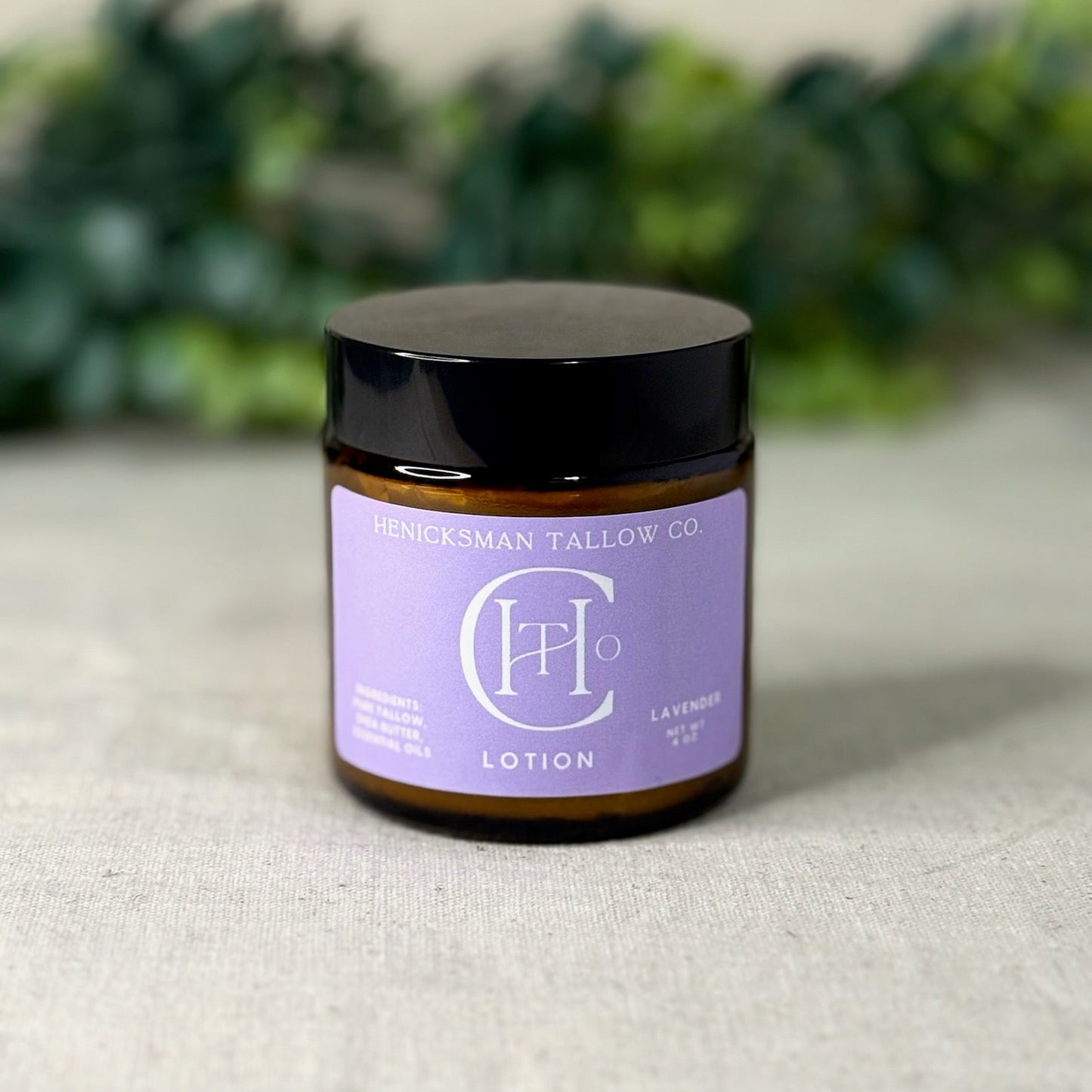 Lotion jar with purple label on a textured surface with greenery in the background