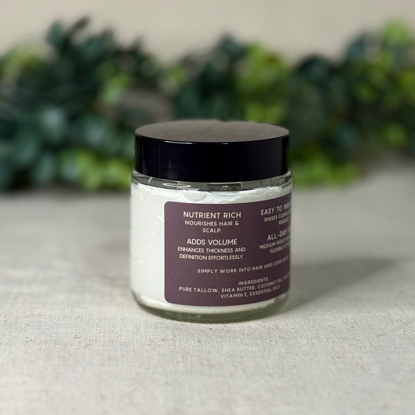 Jar of hair product with a purple label on a textured surface with blurred greenery in the background