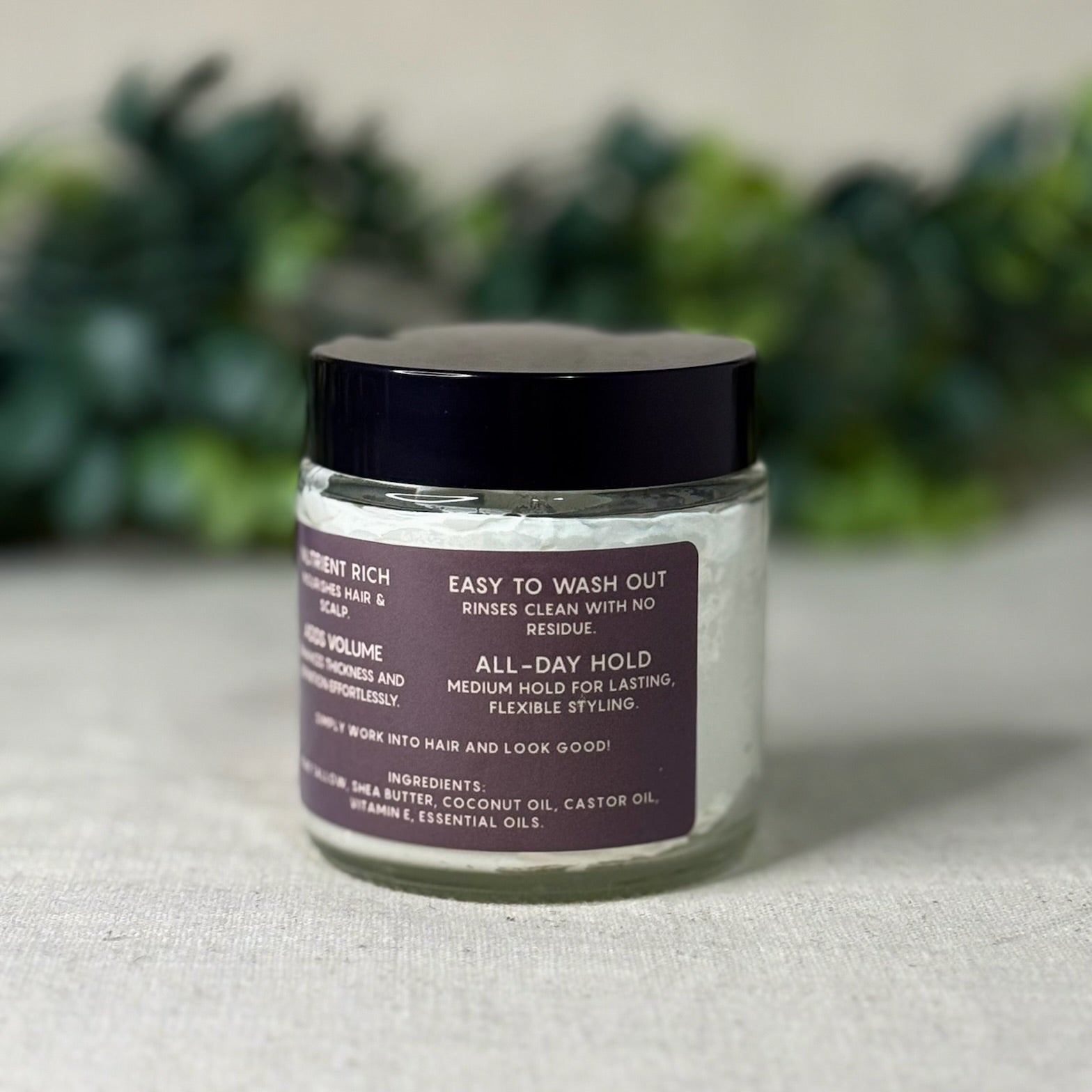 Jar of hair product with a label on a textured surface with greenery in the background