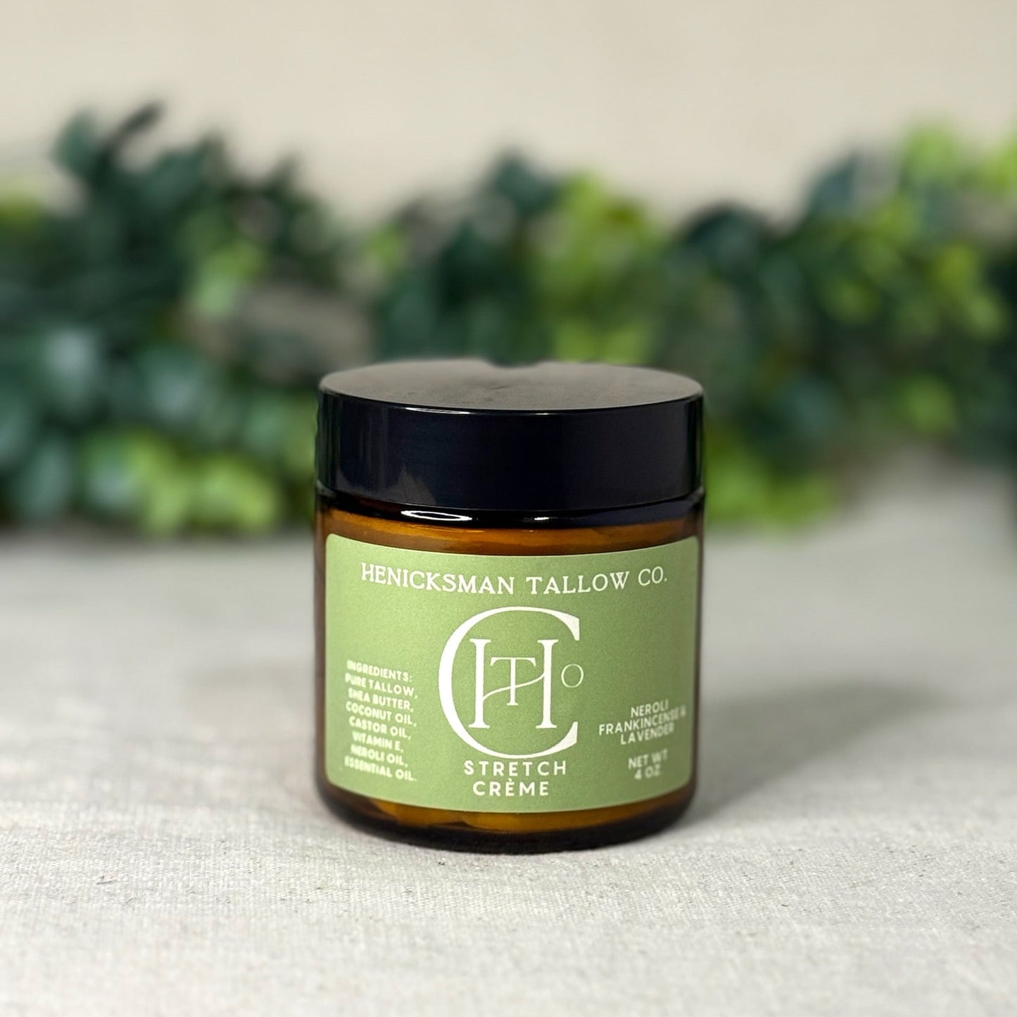 Jar of Henicksman Tallow Co. Stretch Creme on a textured surface with greenery in the background