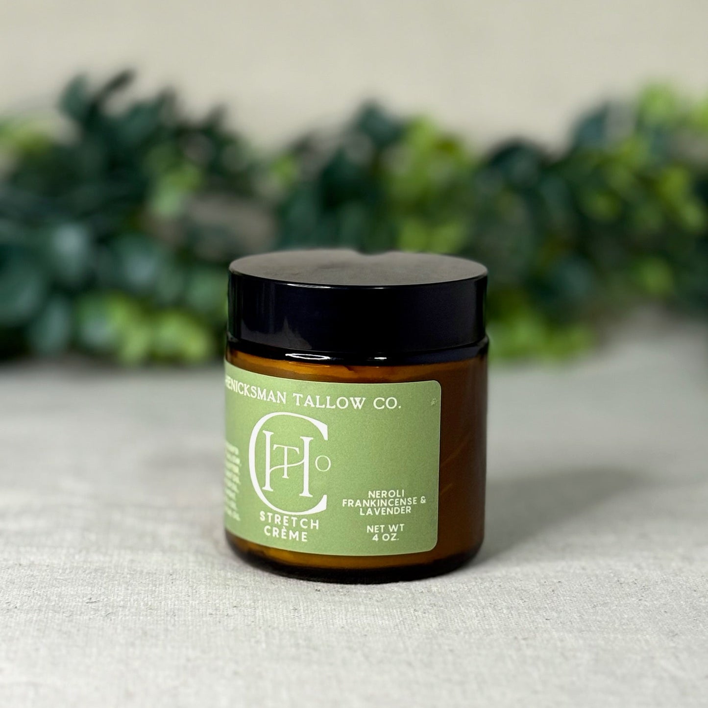 Jar of Stretch Crème from Henicksman Tallow Co. on a textured surface with greenery in the background