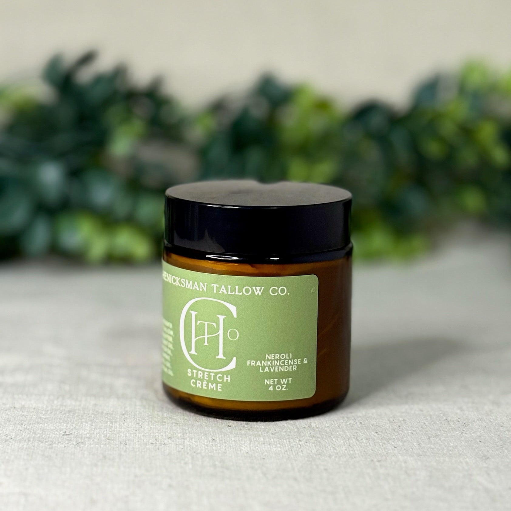 Jar of Stretch Crème from Henicksman Tallow Co. on a textured surface with greenery in the background