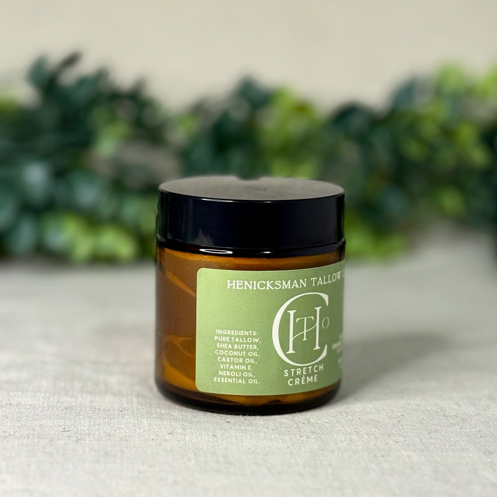 Jar of Henicksman Tallow Stretch Creme on a textured surface with greenery in the background