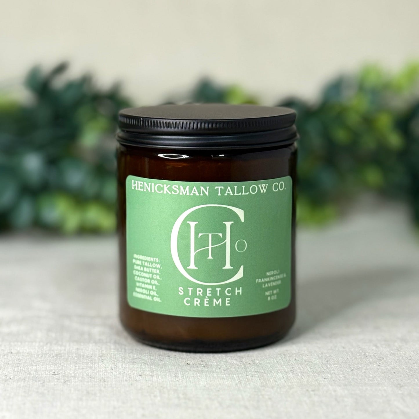 Jar of Henicksman Tallow Co. Stretch Creme on a textured surface with greenery in the background