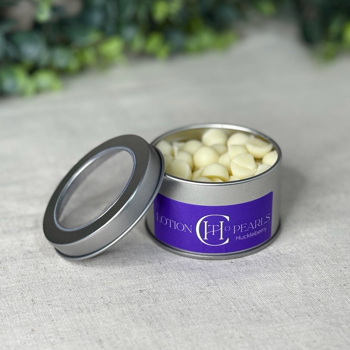 Open tin of Lotion Pearls with a purple label on a textured surface.