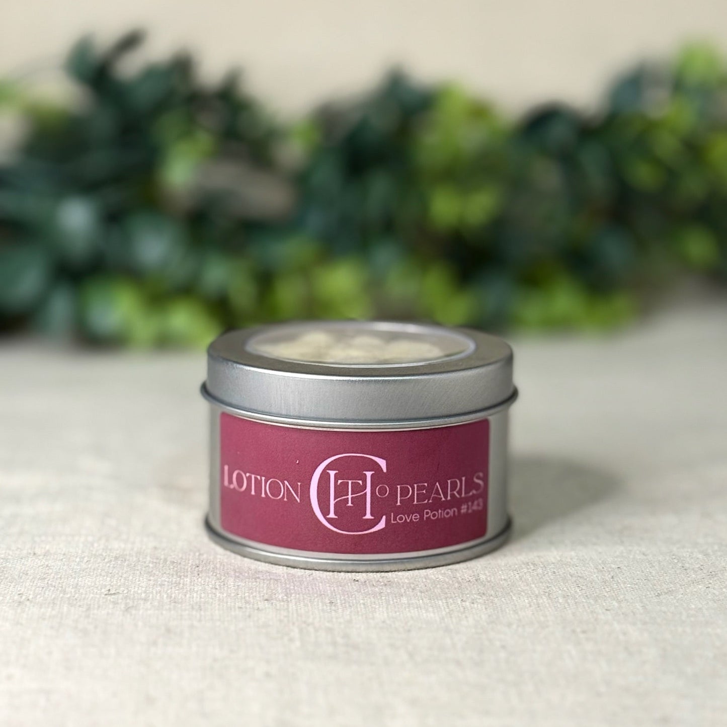 Small tin labeled 'Lotion Pearls' on a textured surface with greenery in the background