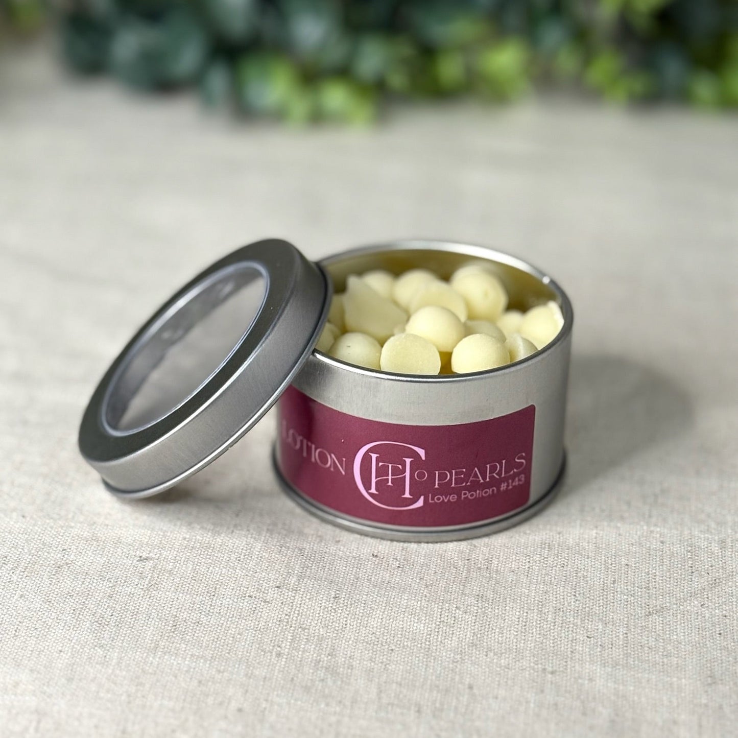 Metallic tin with white pearls on a textured surface with greenery in the background