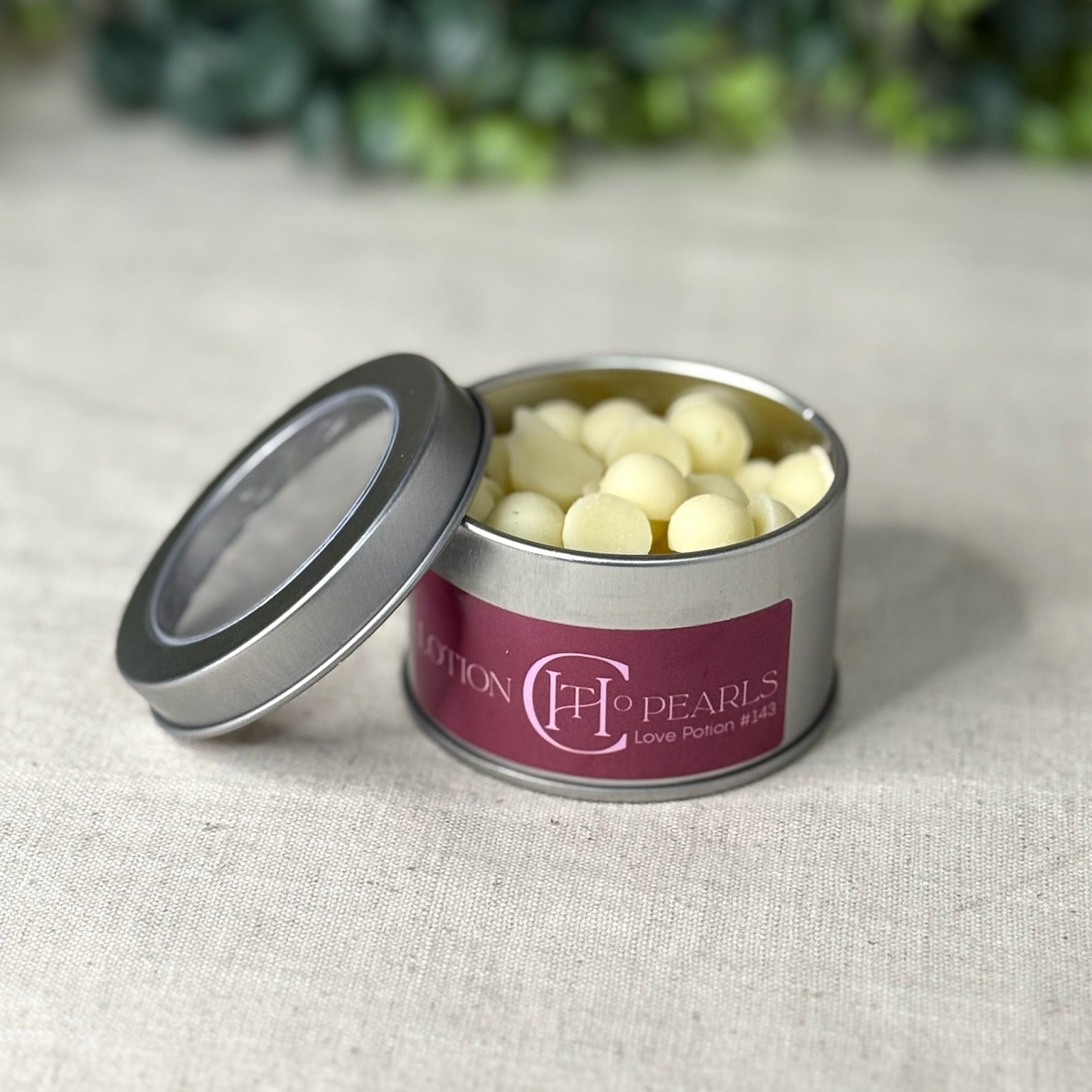 Metallic tin with white pearls on a textured surface with greenery in the background