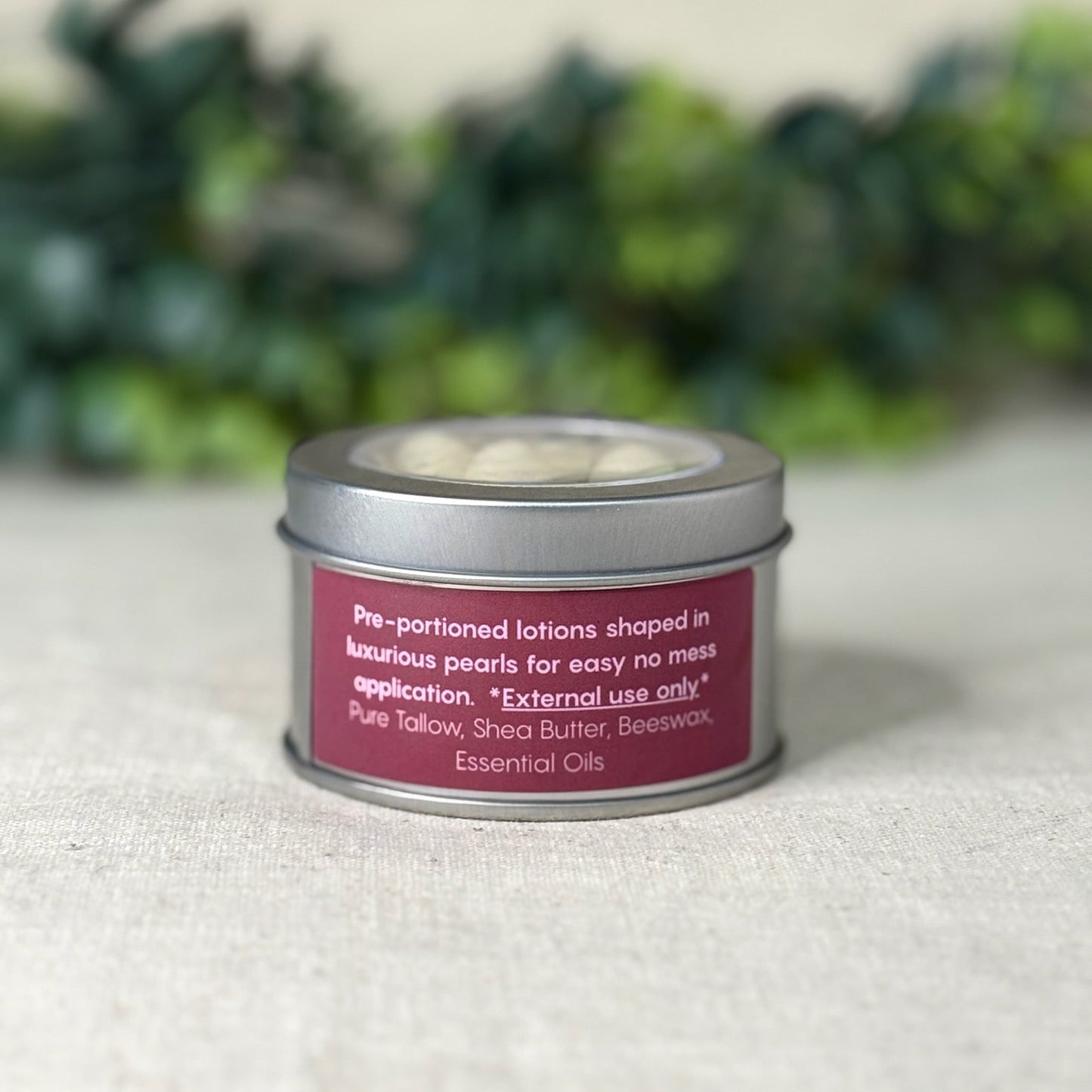 Tin container with a pink label on a textured surface with greenery in the background