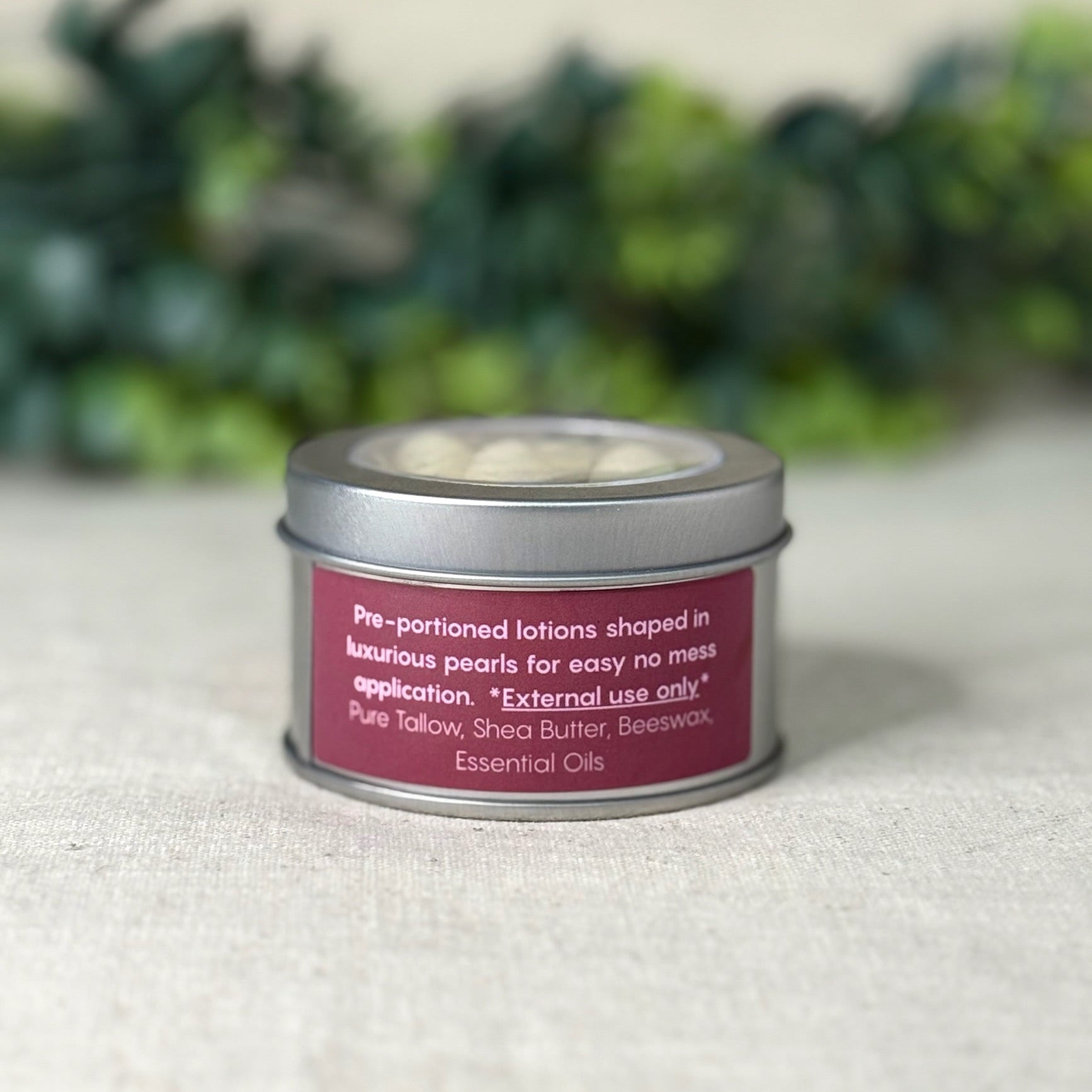 Tin container with a pink label on a textured surface with greenery in the background