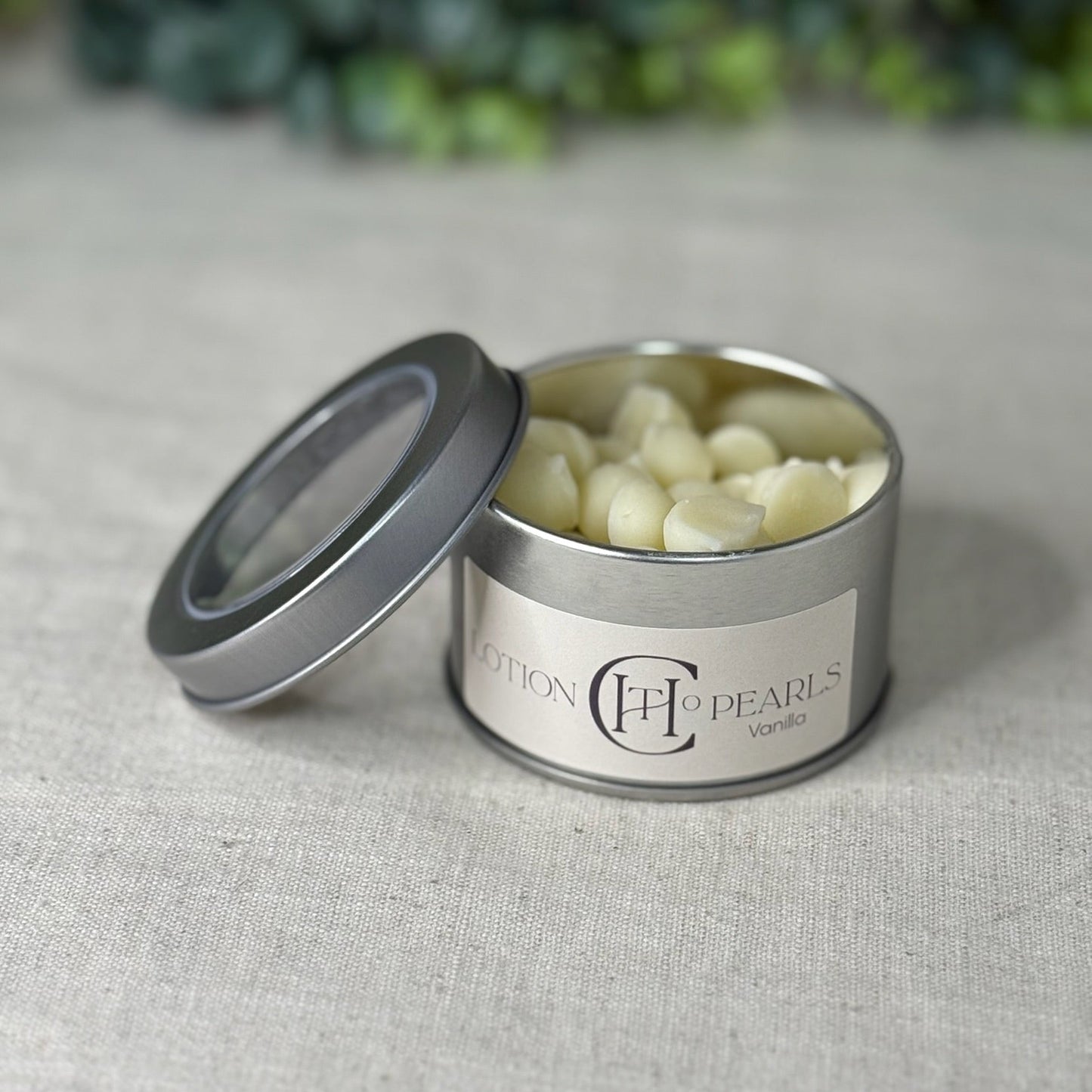 Silver tin with 'CCH Pearls' label containing white pearls on a gray fabric background.