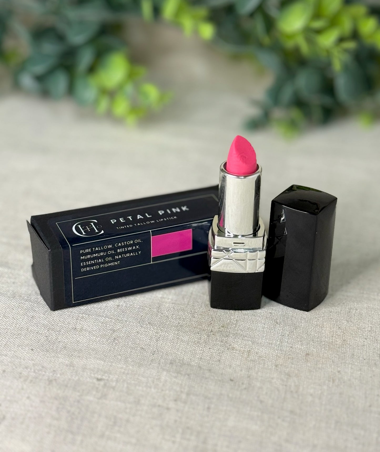 Pink lipstick with black packaging on a textured surface with greenery in the background