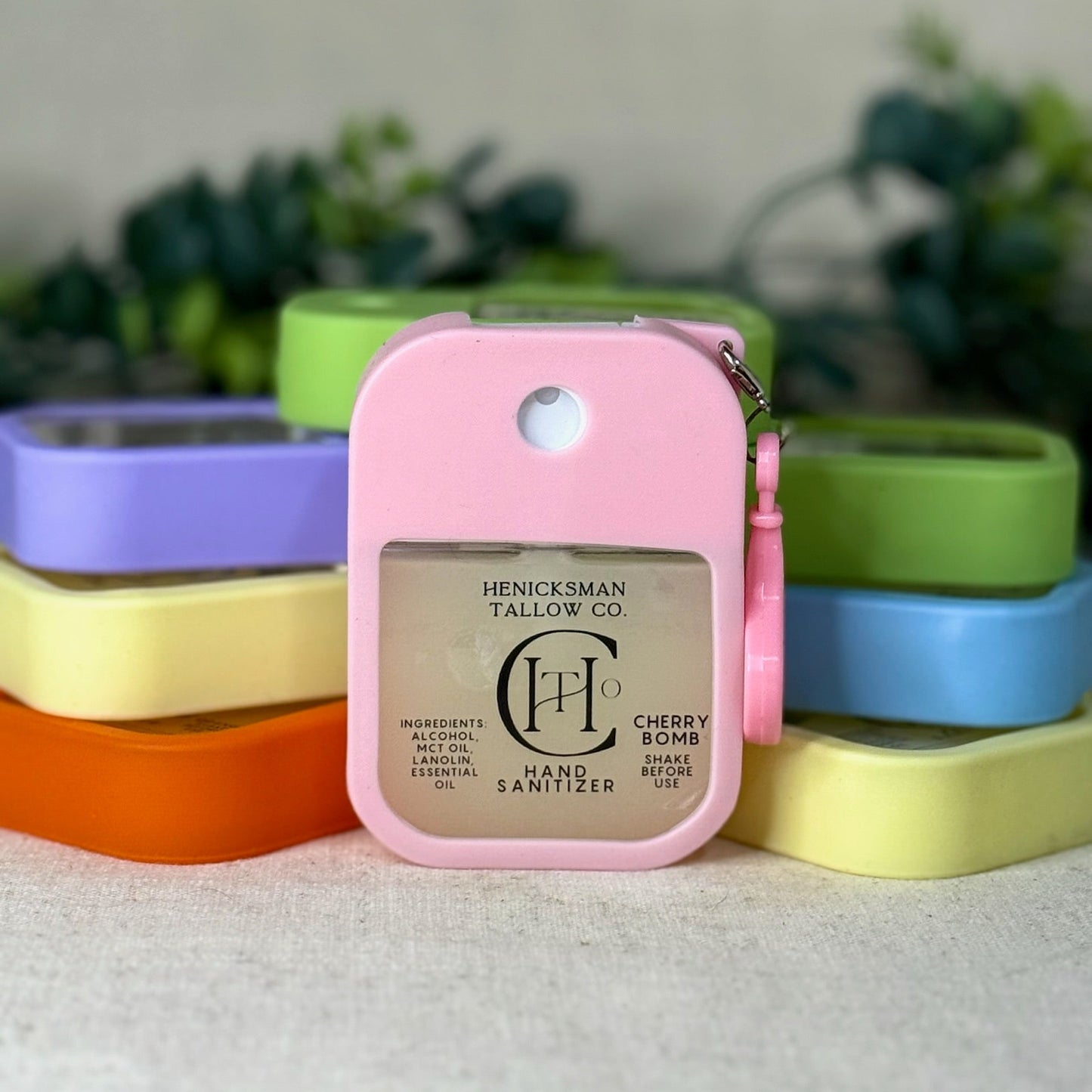 Pink hand sanitizer with brand logo on a white surface with colorful containers in the background
