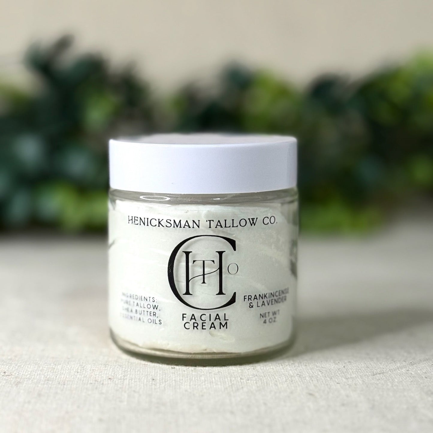 Jar of Henicksman Tallow Co. facial cream on a neutral background with greenery.