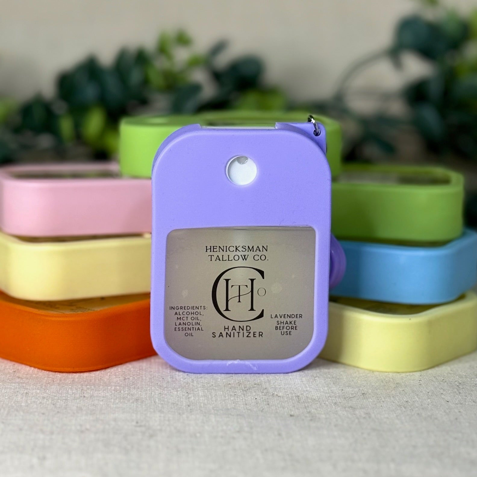 Purple hand sanitizer with brand logo on a white surface with colorful containers in the background.