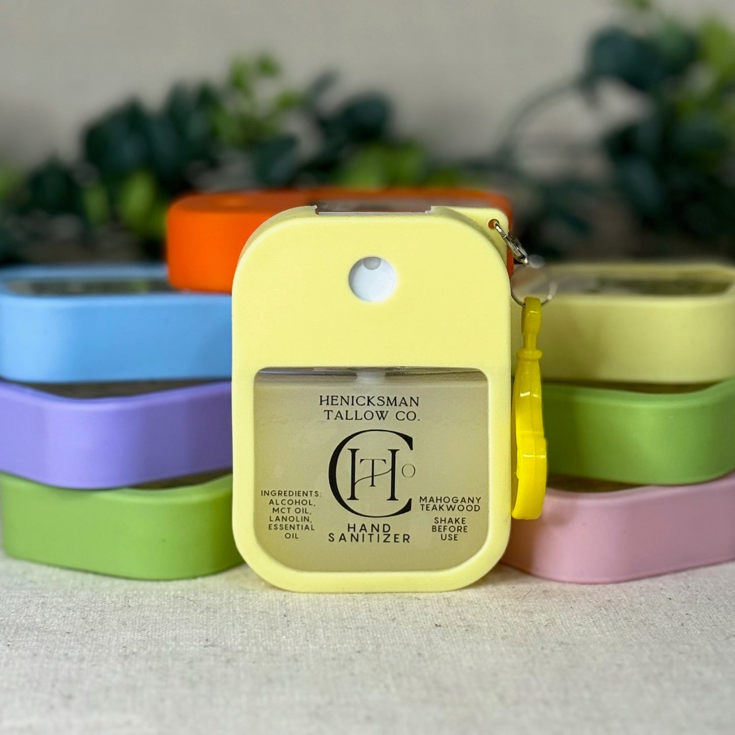 Yellow hand sanitizer with 'Henickman Tallow Co.' branding in front of colorful containers.