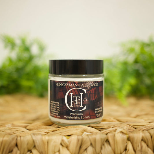 A jar of Henckelsman Tallboy Co CH20 Premium Moisturizing Lotion with a black lid and dark label, resting on a woven straw mat with a blurred green background.